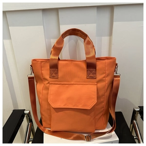 Detail view of large orange nylon tote bag with front pocket on a black chair