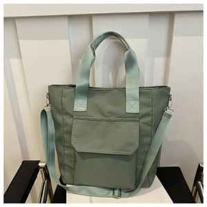 Detail of green nylon tote bag featuring front flap pocket and adjustable shoulder strap