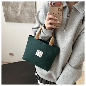 Detailed shot of dark green canvas bucket bag with cartoon bear patch and brown handle