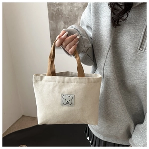 Close-up of canvas bucket bag with brown woven handles and cute bear patch detail
