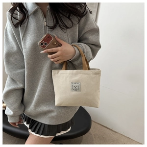 Detail of beige canvas bucket bag with cartoon bear patch and brown contrast handles
