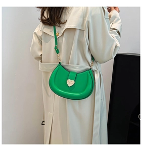 Close-up of vibrant green half-moon crossbody bag featuring a golden heart-shaped buckle
