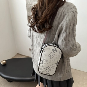Chic white crossbody bag with black letter print and brown trim worn on person