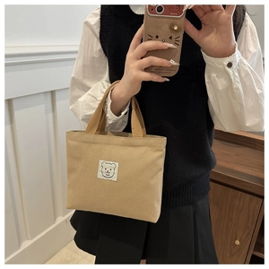 Detail of beige canvas bucket bag with bear patch held by a model in a cozy indoor setting