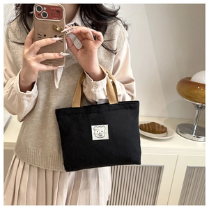 Detail of compact black canvas bag with brown handles and minimalist bear patch