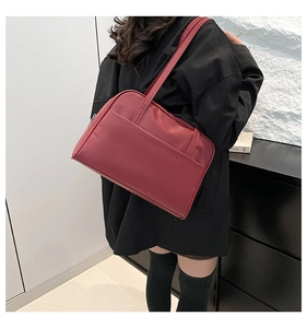 Detail view of large dark red leather shoulder bag worn by model with front pocket
