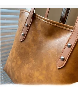 Detail of caramel brown faux leather tote with silver rivets and embossed fashion logo