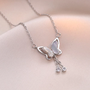 Elegante vlinderketting met parelmoer en zilveren kwastjes op roze zijden achtergrond