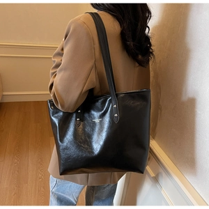 Side view of model wearing a black glossy leather tote bag with white text and silver rivets
