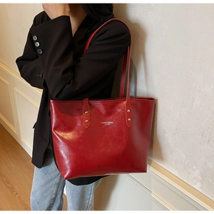Detail of burgundy leather tote bag with white branding and silver metal rivet accents