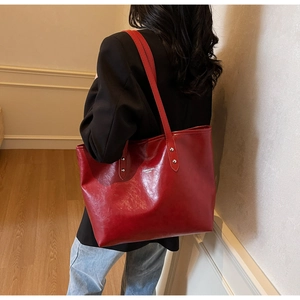 Detailed side view of the large red glossy leather tote bag shown on a model