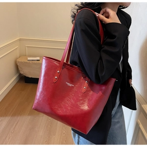 Red large capacity oil skin tote bag worn by a model in a minimalist indoor setting