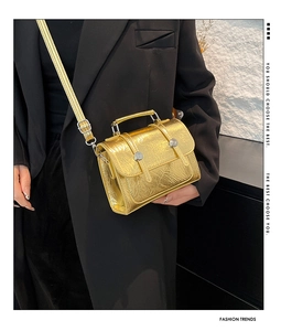 Détail d'un sac bandoulière doré brillant avec poignée métallique porté par un mannequin
