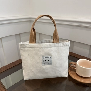 Mini canvas tote bag with bear patch and brown handles in a cozy cafe setting