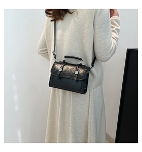 Detail of black glossy crossbody bag with wrinkled texture and silver buckles on model