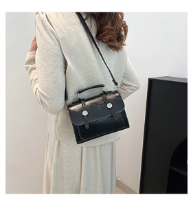 Detail of a vintage black textured crossbody bag with silver buckles worn by a model