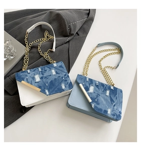 Detail von ausgefranstem Denim-Überschlag mit Metallkette und Riemen an den Umhängetaschen