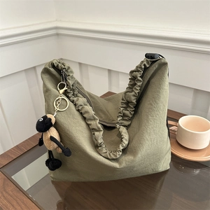 Detail of army green pleated tote bag with a small plush sheep pendant on wooden table