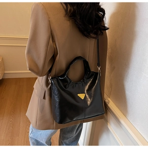 Detail of black glossy bucket bag featuring gold triangle hardware and shoulder strap