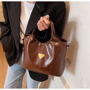 Detail of a dark brown PU leather bucket bag with a gold triangular metal emblem