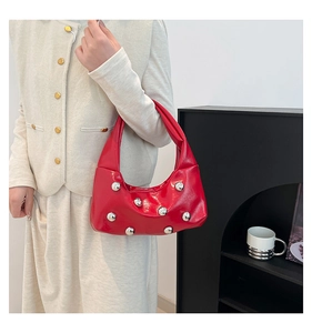 Detail of red glossy hobo bag with silver metallic studs worn with beige knitwear