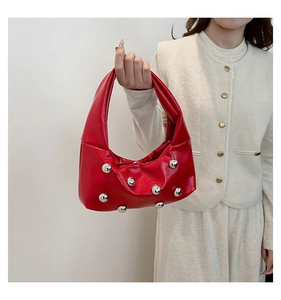 Détail d'un sac demi-lune en cuir rouge brillant avec rivets argentés et poignée solo