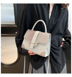 Detail of light gray crocodile texture handbag with gold metal bar and shoulder strap
