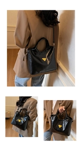 Detail view of black glossy tote bag featuring a yellow triangular metal logo and handle