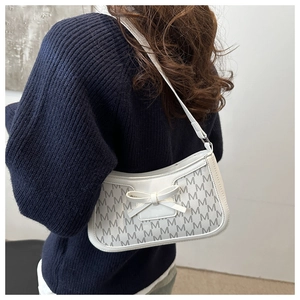 Close-up of elegant white underarm bag featuring a classic bow and letter M pattern