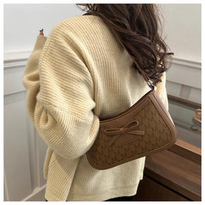 Close-up of brown monogram underarm bag with leather bow on a model wearing beige sweater