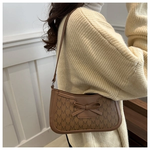 Detail of a brown baguette bag with 'M' monogram and a decorative front bow