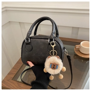 Detail der schwarzen Lederhandtasche mit geprägten Buchstaben und Plüschbär-Anhänger