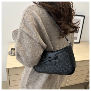 Close-up of black baguette bag with M-letter print and leather bow on knit sweater