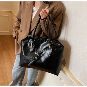 Detail of black glossy leather tote bag with gold hardware and slim shoulder strap