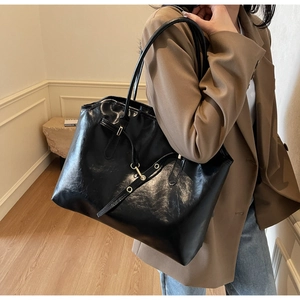 Detail view of large black tote bag with glossy leather finish and gold ring accent