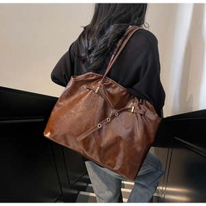 Detail view of a large brown vintage tote bag with buckle straps worn by a model