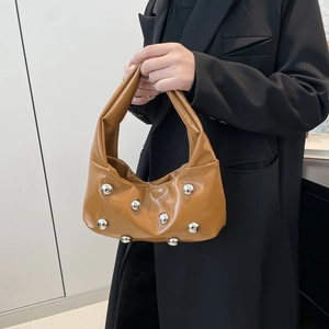 Sac hobo en cuir marron avec rivets argentés porté par un mannequin en costume noir