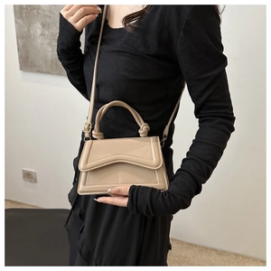Detail of beige glossy crossbody bag featuring a wavy flap and knotted top handle