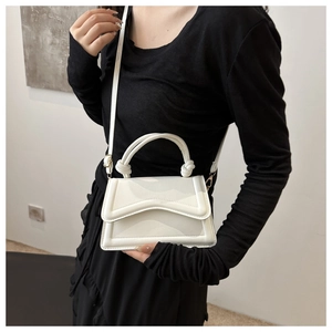 Minimalist white faux leather mini handbag with knot handle worn by a model in black dress