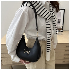Detail of minimalist black hobo bag with a golden metal bow and slender leather strap