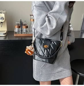 Détail du sac seau noir matelassé avec fermoir doré sur fond de café moderne
