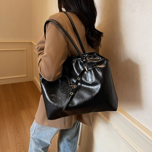 Large black shiny leather tote bag shown on model in a stylish indoor setting