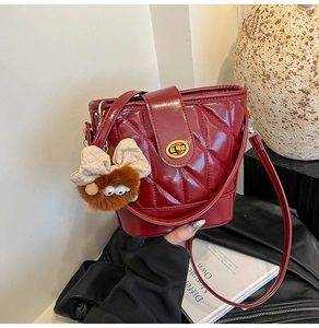 Détail du sac seau rouge matelassé avec fermoir rotatif doré et breloque en peluche