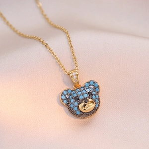 Macro view of gold teddy bear pendant with turquoise stones on pink silk background