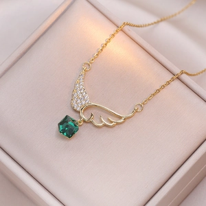 Collier élégant ailes d'ange dorées avec pierre émeraude sur un écrin à bijoux beige doux