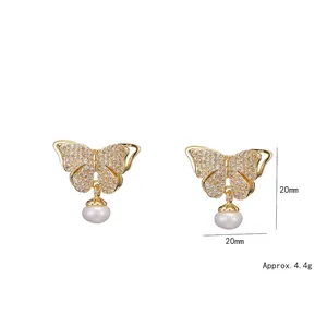 Boucles d'oreilles papillon dorées avec zircons et perles d'eau douce sur fond blanc
