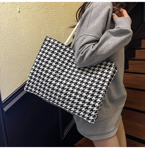 Side view of large houndstooth tote bag worn by model against a stylish interior background