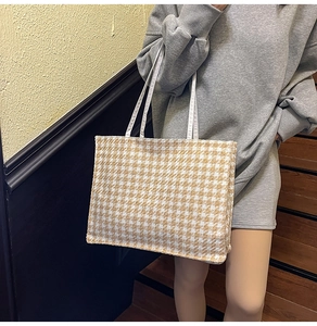 Close-up of houndstooth wool tote bag with slim white shoulder straps on wooden stairs