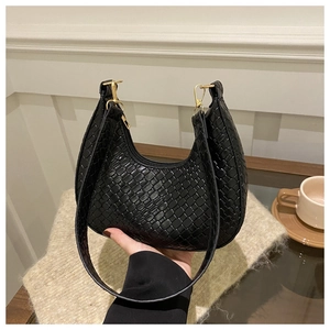 Detail of black woven leather crescent hobo bag with gold hardware on wooden desk