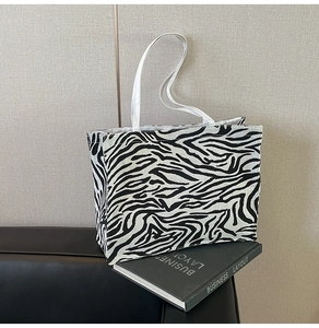 Detail of zebra pattern tote bag placed on a leather sofa with a book accessory